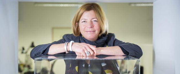 Dame Laura Lee leaning on an architect's model of a Maggie's centre and smiling at the camera