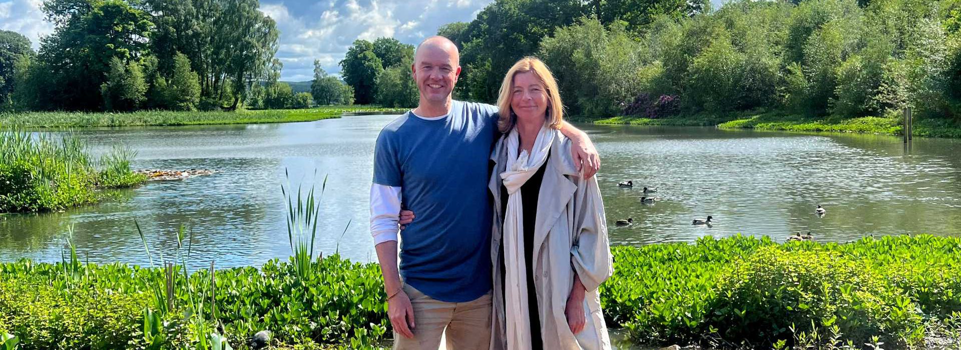 Dame Laura Lee and Darren Hawkes standing shoulder to shoulder in front of the Maggie's Forth Valley lake