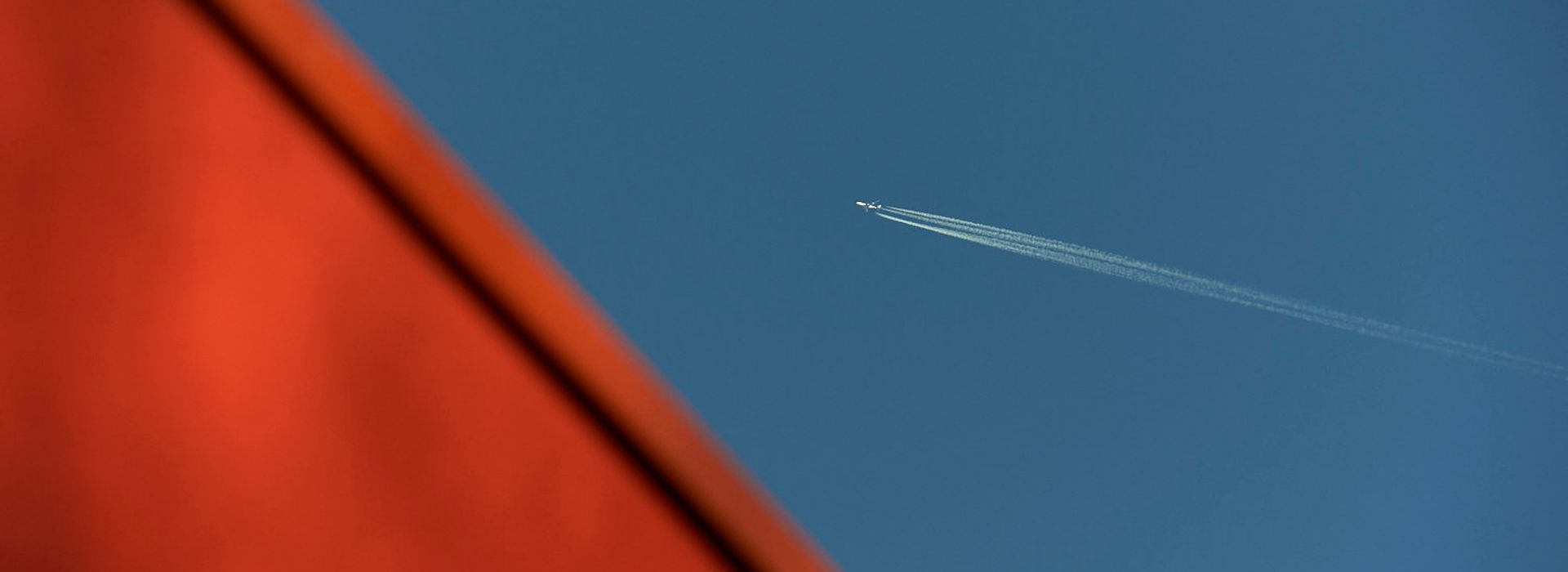 Abstract photo of orange roof of Maggie's West London and blue sky with plane flying over